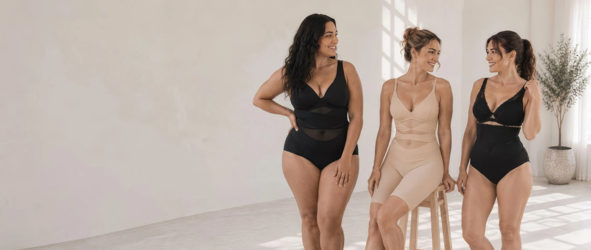 Three women modeling shapewear and black lingerie in a bright, minimalist studio with large windows and a potted plant.