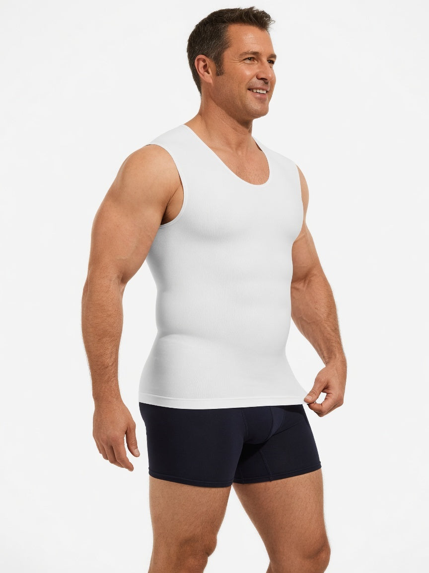 A muscular man wearing a white sleeveless compression tank top and dark navy boxer briefs, standing against a light gray studio background.